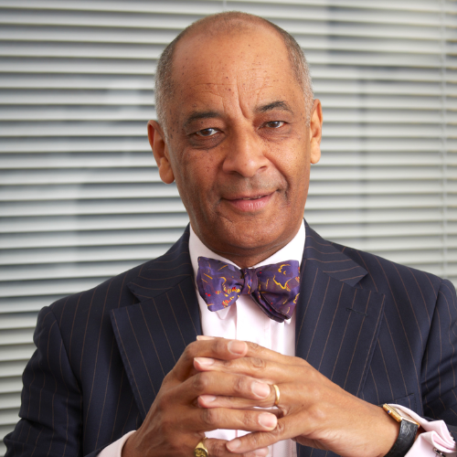 Sir Kenneth Olisa - a biracial Black British man in his early 70s, wears a brightly coloured purple bow tie and navy blue suit.